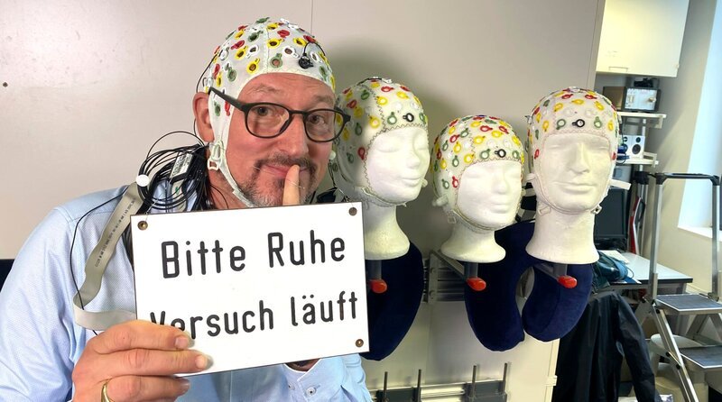 Eckart von Hirschhausen (Mitte) bereitet sich mit einer EEG-Haube auf ein Gedanken-Experiment im Leibniz-Institut für Neurobiologie Magdeburg vor. – Bild: MDR/​Jan Tenhaven