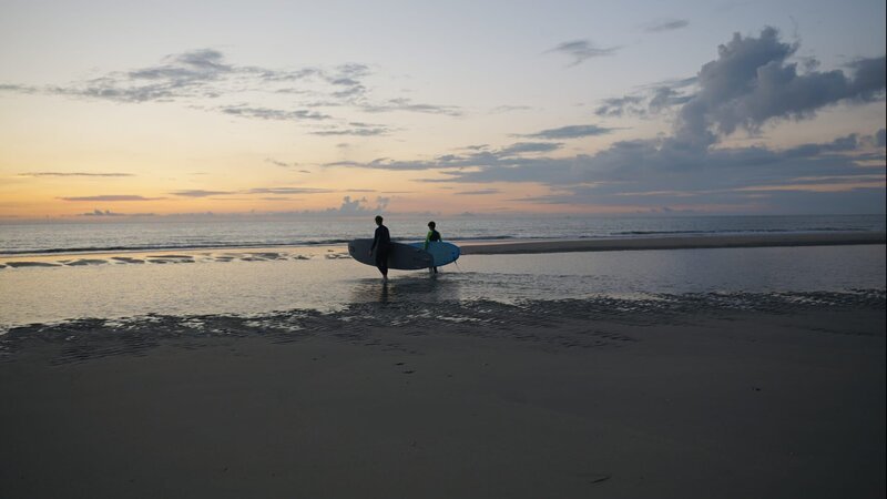 Jula (l.) und Christoph (r.) gehen bei Sonnenuntergang surfen. – Bild: ZDF und Finn Sasse.