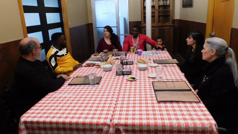 Kobe’s friend Temperture joins Emily and her family for lunch and discuss the role of husbands and wives in their culture. – Bild: Warner Bros. Discovery