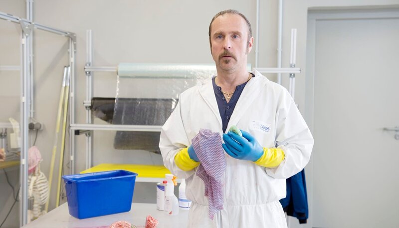 In einem Forschungsinstitut für Biotechnik kam ein Mann bei einem Experiment ums Leben. Schotty (Bjarne Mädel) soll das Blut wegputzen. – Bild: NDR/​Thorsten Jander