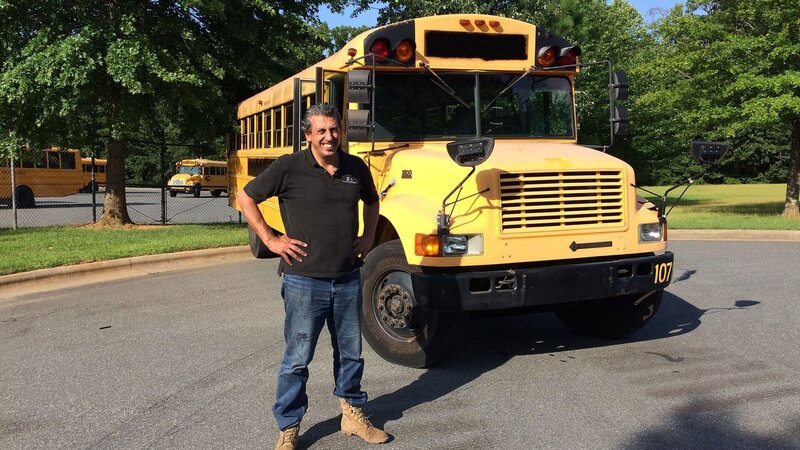 Michael Manousakis standing in front of the yellow school bus. – Bild: 2020 DISCOVERY DEUTSCHLAND