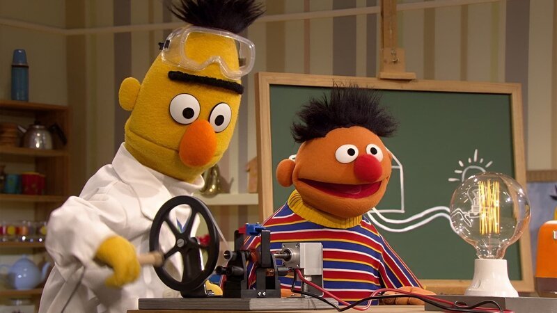 Bert (l.) möchte Ernie (r.) zeigen, wie ein Stromkreis funktioniert. – Bild: NDR/​Studio Hamburg Produktion/​Sesame workshop