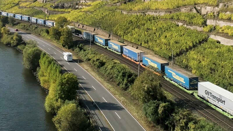 Ein Güterzug fährt entlang einer Straße und eines Flusses. – Bild: Längengrad Filmproduktion/​BR