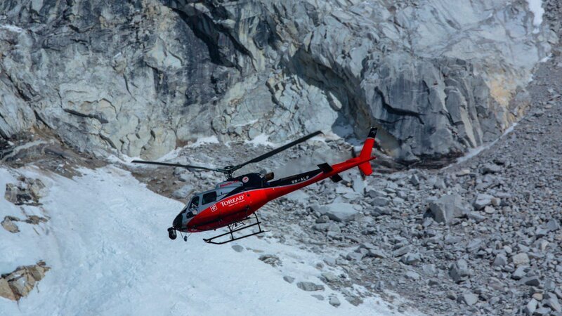 Helicopter flies with snow and rock behind it. – Bild: International Networks /​ Discovery Communications