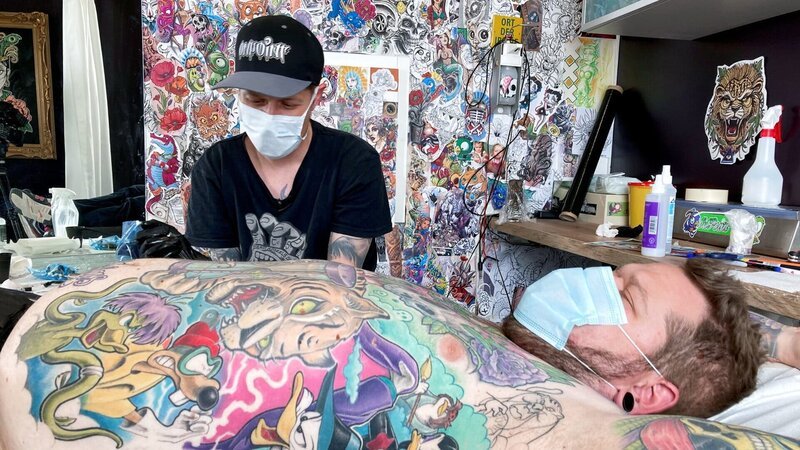 Dominik Dietrich (vorne) bei seinem Tätowierer Fabe in St. Gallen: Beide mögen Cartoons und viel Farbe – Bild: SRF Dominik Dietrich (vorne) bei seinem Tätowierer Fabe in St. Gallen: Beide mögen Cartoons und viel Farbe – Bild: SRF