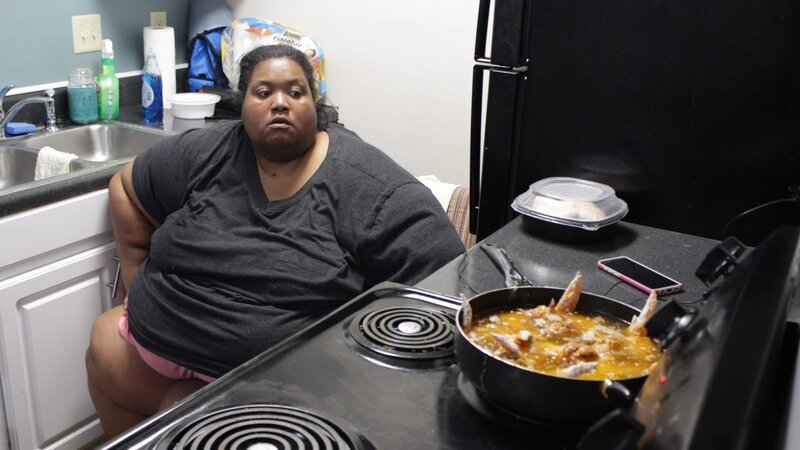 Kelly sitting in front of a stove cooking. – Bild: Discovery Communications.