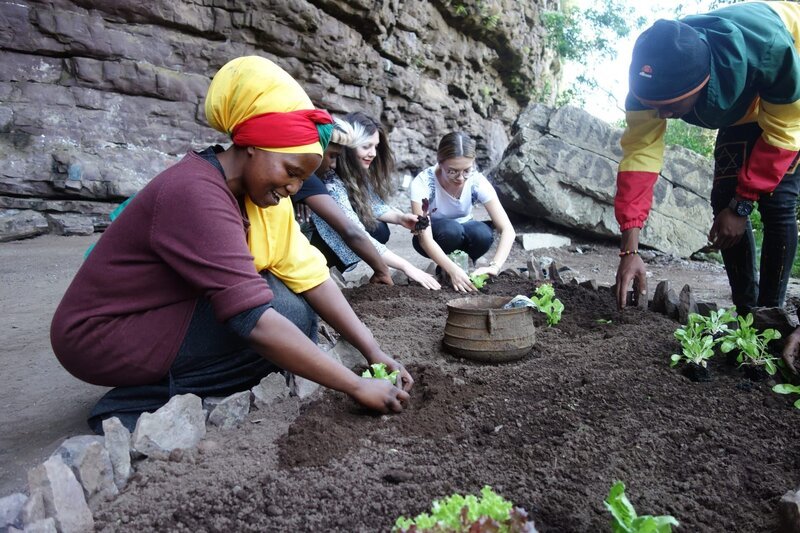Dass die Rastafari-Kultur sehr eng mit der Natur verbunden ist, lernen die Praktikantinnen der „Weißen Lady“, Theresa und Lena, beim gemeinsamen Anpflanzen von Gemüse mit Gläubigen in einer Felsenhöhle in Kwazulu-Natal. – Bild: BR/​Farah M’haimdat