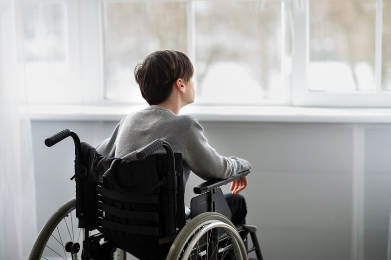 Back view of disabled teenager in wheelchair looking out window – Bild: Shutterstock /​ Prostock-studio