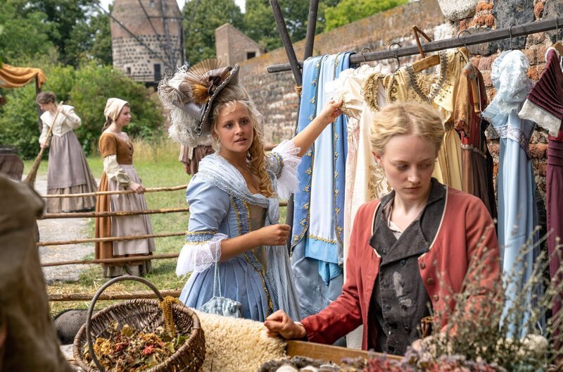 Prinzessin Josefine (Lucie Hollmann) entdeckt auf dem Markt die schönen Kleider von Helene (Caroline Hellwig). – Bild: WDR/​Wolfgang Ennenbach