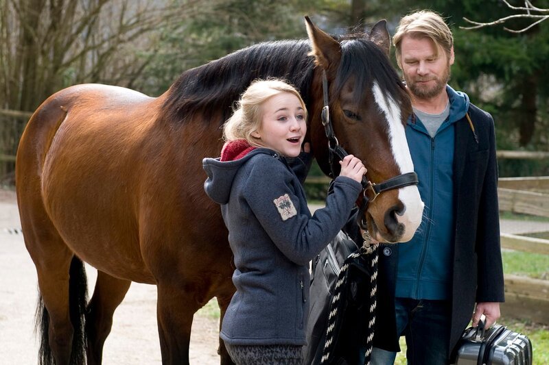 Nelly (Jule-Marleen Schuck) freut sich über das Pferd das sie von ihrem Vater (Kai Scheve) geschenkt bekommen hat. – Bild: SWR/​Maria Wiesler