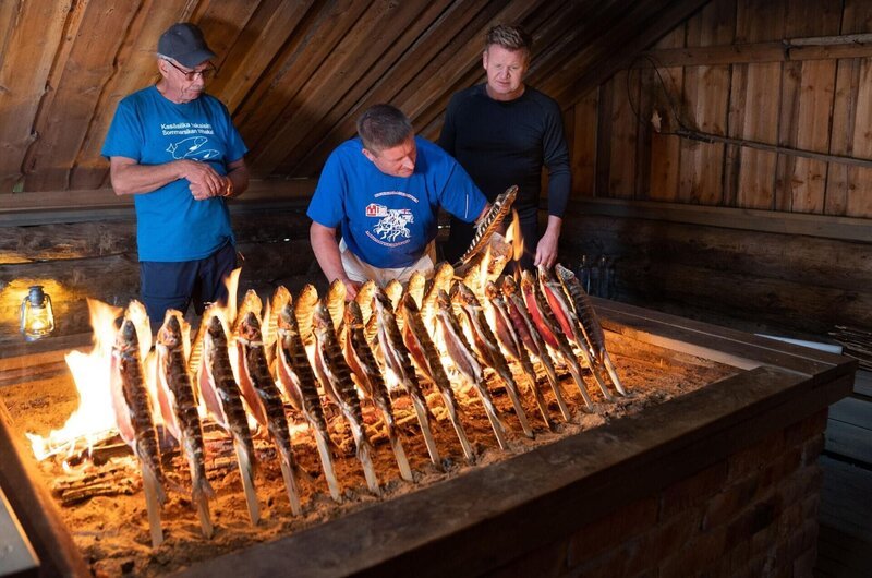Finland – L to R: Marku and Kimmo teach Gordon Ramsay the traditional way to cook whitefish. After resting for 24 hours, the fish are roasted on sticks over an open fire. (Credit: National Geographic/​Justin Mandel) – Bild: Studio Ramsay and All3Media International Lizenzbild frei