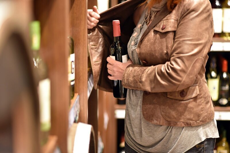 shoplifting – a woman steals a bottle of wine in a supermarket – Bild: 2019 Shutterstock