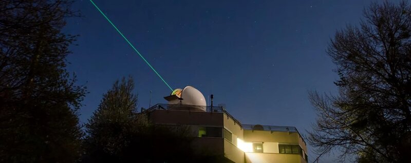 Die Satellitenstation Graz-Lustbühel. Der grüne Laserstrahl ortet gerade Weltraumschrott. – Bild: ServusTV /​ Bilderfest
