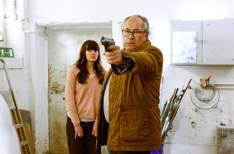 Daniela (Alice Gruia, l.) sucht Schutz hinter Klaus (Hartmut Volle, r.), der mit gezogener Waffe, den Entführern entgegentritt. – Bild: ARD/​Kai Schulz