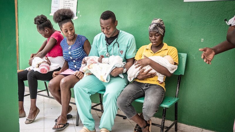 Der 24-jährige Geburtshelfer Edouard in einem Krankenhaus im Süden Haitis, umringt von Frauen und deren Neugeborenen – Bild: Anja Booth /​ © Anja Booth
