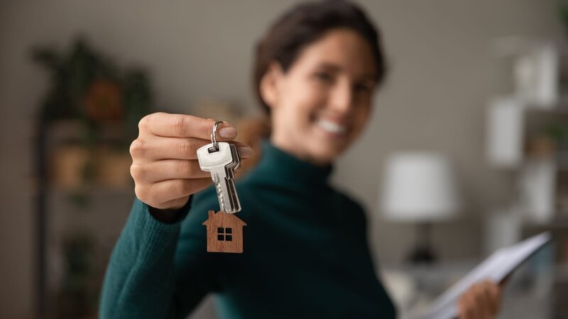 Close up focus on keys, smiling woman realtor selling apartment, offering to client, showing at camera, holding documents, contract, making purchasing deal, real estate agent, mortgage or rent – Bild: Shutterstock /​ Shutterstock /​ Copyright (c) 2021 fizkes/​Shutterstock. No use without permission.