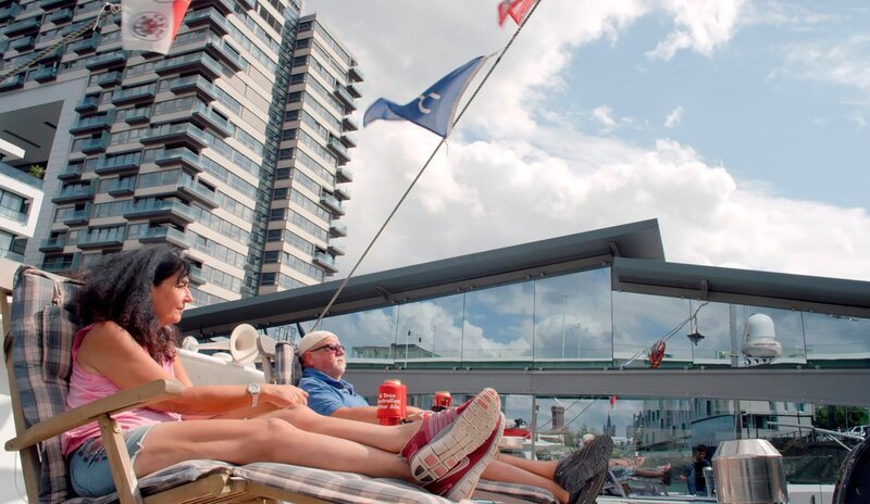 Nordrhein-Westfalen im Hochsommer. Ein Land im Hitzemodus. Auch bei Höchsttemperaturen arbeiten die Menschen weiter, treiben Sport und suchen den Schatten. Für die einen traumhafte Bedingungen, für die anderen Quälerei in brütender Sonne. Autorin Eva Schötteldreier zeigt in diesem Film, wie sich so ein perfekter Sommertag anfühlt. Immer auf der Suche nach den schönsten Geschichten, mit aufwendiger Kameratechnik unter strahlend blauem Himmel. – Das etwas andere Wochenendhaus. – Martina (l) und Eddie Allnoch im Kölner Rheinauhafen auf ihrem historischen Aalschokker. – Bild: WDR/Gruppe 5 Filmproduktion/Adnane Korchyou Nordrhein-Westfalen im Hochsommer. Ein Land im Hitzemodus. Auch bei Höchsttemperaturen arbeiten die Menschen weiter, treiben Sport und suchen den Schatten. Für die einen traumhafte Bedingungen, für die anderen Quälerei in brütender Sonne. Autorin Eva Schötteldreier zeigt in diesem Film, wie sich so ein perfekter Sommertag anfühlt. Immer auf der Suche nach den schönsten Geschichten, mit aufwendiger Kameratechnik unter strahlend blauem Himmel. – Das etwas andere Wochenendhaus. – Martina (l) und Eddie Allnoch im Kölner Rheinauhafen auf ihrem historischen Aalschokker. – Bild: WDR/Gruppe 5 Filmproduktion/Adnane Korchyou