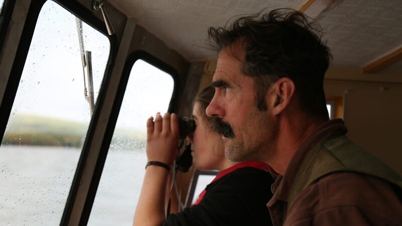 Ray and his daughter looking out of the boat windows with a binocular. – Bild: Animal Planet /​ Discovery Communications