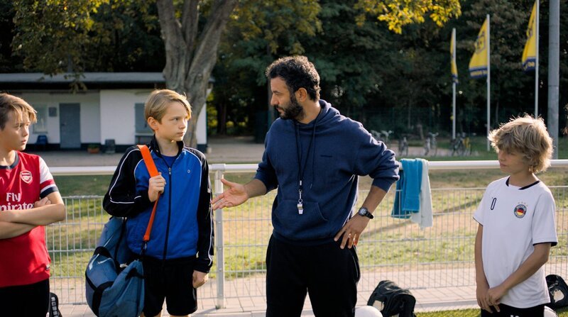 Trainer Rainer (Mohamed Achour) stellt Ben (Yoran Leicher) der Mannschaft des SC Düren vor. – Bild: BR/NDR/Weydemann Bros. GmbH/Monika Plura Trainer Rainer (Mohamed Achour) stellt Ben (Yoran Leicher) der Mannschaft des SC Düren vor. – Bild: BR/NDR/Weydemann Bros. GmbH/Monika Plura