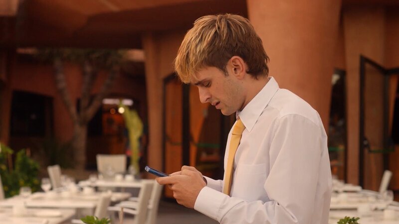 Mit wem kommuniziert Hotelpage Iker (Guillermo Campra) per Handy? – Bild: Dancing Ledge Production
