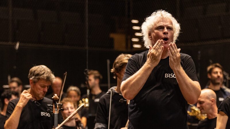 Über 500 Blasmusiker und Blasmusikerinnen folgten der Einladung, Sir Simon Rattle (im Bild) und das Symphonieorchester des Bayerischen Rundfunks bei einer Probe von Mahlers 6. Symphonie zu besuchen. In der Isarphilharmonie verfolgten Ensembles, die sich für eine Teilnahme am „Symphonischen Hoagascht“ beworben hatten, aufmerksam das Probengeschehen. – Bild: Markus Konvalin /​ BR /​ BR/​Markus Konvalin