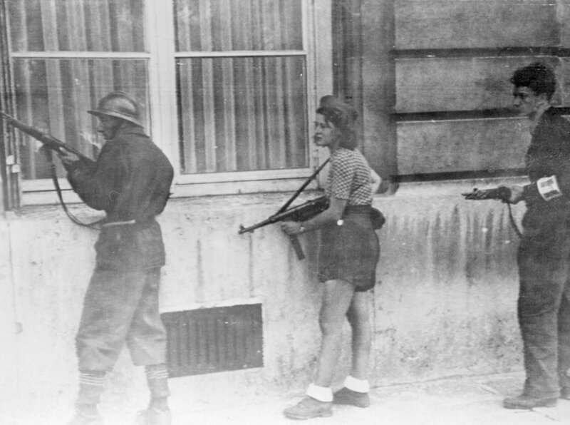 (Originalbildunterschrift) 28.8.1944-Paris, Frankreich: Diese junge Französin in ihrer Einsatzkleidung hält sich dicht an einer Mauer und hält ihre Maschinenpistole bereit, um im Handumdrehen zu schießen. Sie gehört zu einer Patrouille, die deutsche Scharfschützen aufspüren soll, die sich noch in Paris verstecken. – Bild: Perpetual Entertainment /​ THE HISTORY CHANNEL/​Bettmann/​Bettmann