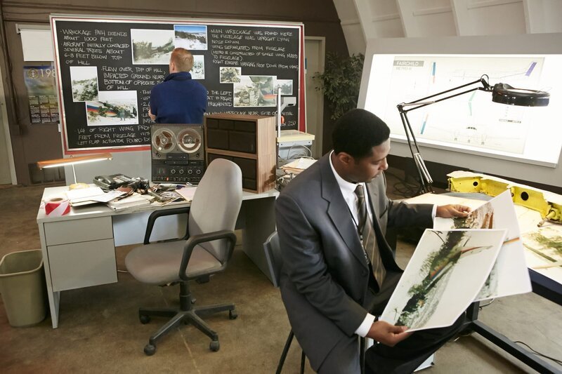 RE-CREATION: Tom Haueter (played by Danny Deakin) looks over the notes the investigators have been keeping on the blackboard while another investigator (played by a background performer) looks over photos of the wreckage.   (photo credit: Cineflix/​Ian Watson) – Bild: Copyright © The National Geographic Channel.