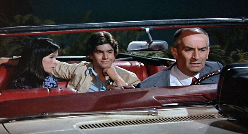 In der Pinienkrone hoch über dem Meer erfahren Henri (Louis de Funes) und seine ungebetenen Mitfahrer (Geraldine Chaplin und Olivier de Funes) in der abendlichen Nachrichtensendung, dass sie vermisst werden. – Bild: RTL / © 1971 STUDIOCANAL – PEGASO S.R.L. In der Pinienkrone hoch über dem Meer erfahren Henri (Louis de Funes) und seine ungebetenen Mitfahrer (Geraldine Chaplin und Olivier de Funes) in der abendlichen Nachrichtensendung, dass sie vermisst werden. – Bild: RTL / © 1971 STUDIOCANAL – PEGASO S.R.L.