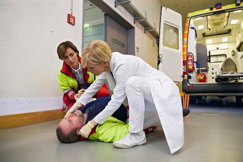 Die beiden Rettungssanitäter Susanne Scholz (Dorothea Arnold, oben li.) und Jörg Frost (Felix Vörtler, liegend) wollen einen Patienten einliefern,da kippt Jörg plötzlich um. Dr. Kathrin Globisch (Andrea Kathrin Loewig, oben re.) ist sofort zur Stelle. – Bild: MDR/​Saxonia Media Filmproduktion/​Wernicke