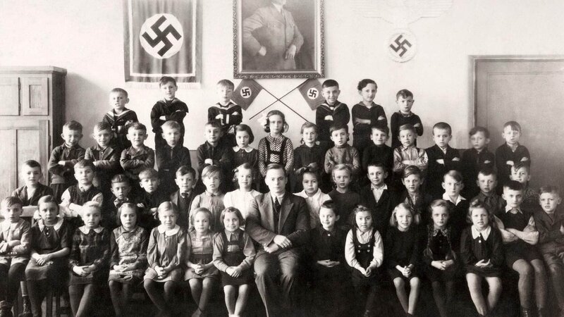 Ein Klassenporträt von jungen Schulkindern mit ihrem Lehrer vor einer Fotografie von Adolf Hitler und zwei Hakenkreuzen während des Zweiten Weltkriegs, um 1940. – Bild: RTL