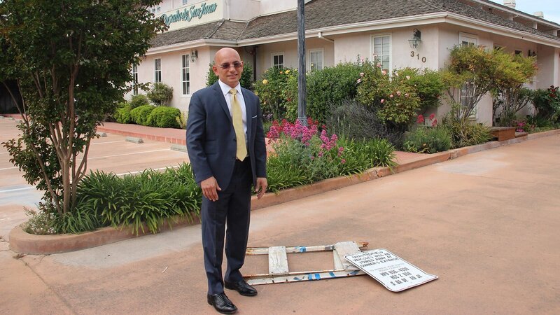 Host Anthony Melchiorri stands next to a broken sign outside the Posada de San Juan in San Juan Bautista, California. – Bild: The Travel Channel, L.L.C.