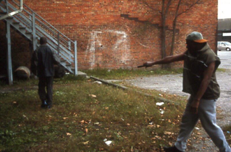 Ein Mitglied der Straßengang „K Street Crew“ zielt mit einer Pistole auf den Mann. – Bild: National Geographic