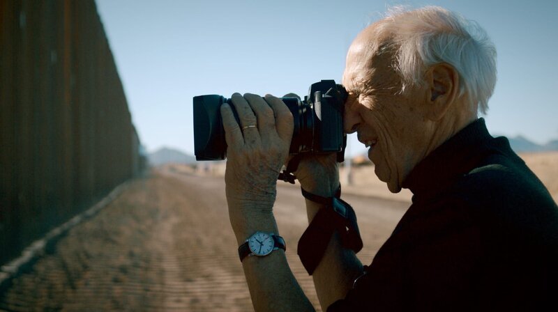 Im Jahr 2017 erhielt der Fotograf Thomas Hoepker die Diagnose Alzheimer. Während seine Fotokunst zu einem kollektiven Gedächtnis wurde, entschwindet ihm allmählich sein eigenes. Sein letzter großer Traum: Ein Roadtrip durch die USA mit seiner Ehefrau. Eine Neuauflage jener Reise, die seine internationale Karriere als Fotograf begründet hat. – Thomas Hoepker vor dem Grenzzaun zwischen den USA und Mexiko in Douglas, New Mexico. – Bild: HR/​rbb/​NDR/​GRANVISTA Media/​DCM/​Florian Mag