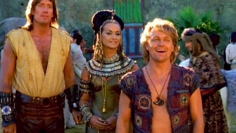 Hercules (Kevin Sorbo, li.) und Iolaus (Michael Hurst) besuchen Königin Nefertiti (Gabriella Larkin) in Ägypten. Iolaus ist überglücklich wieder in Ägypten zu sein und nervt alle mit seinem Wissen über die ägyptische Kultur. – Bild: TVNOW