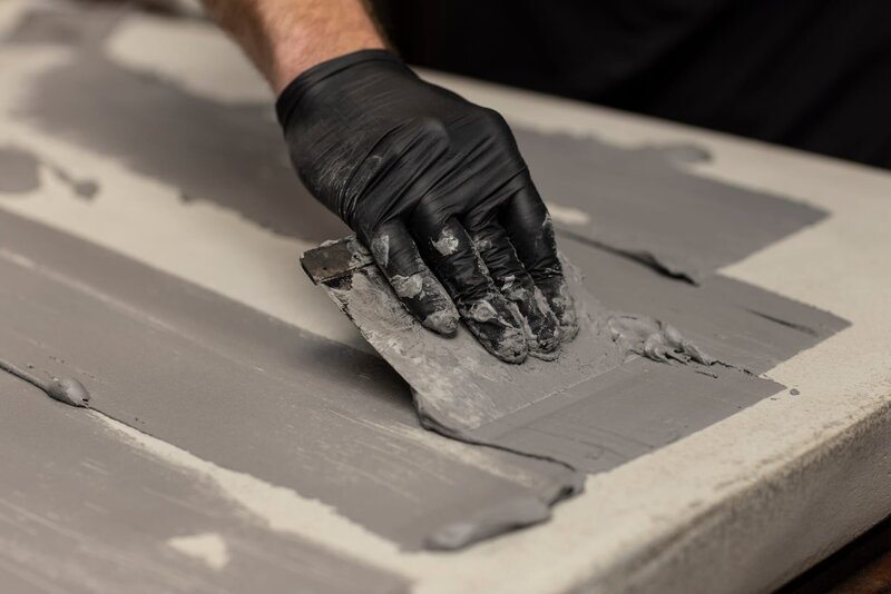 Beton Cire wird von einer Hand getragen, die Gummihandschuhe und ein Putty-Messer trägt, wodurch eine neue graue, stylische Oberfläche entsteht. – Bild: Lea Rae/​Shutterstock