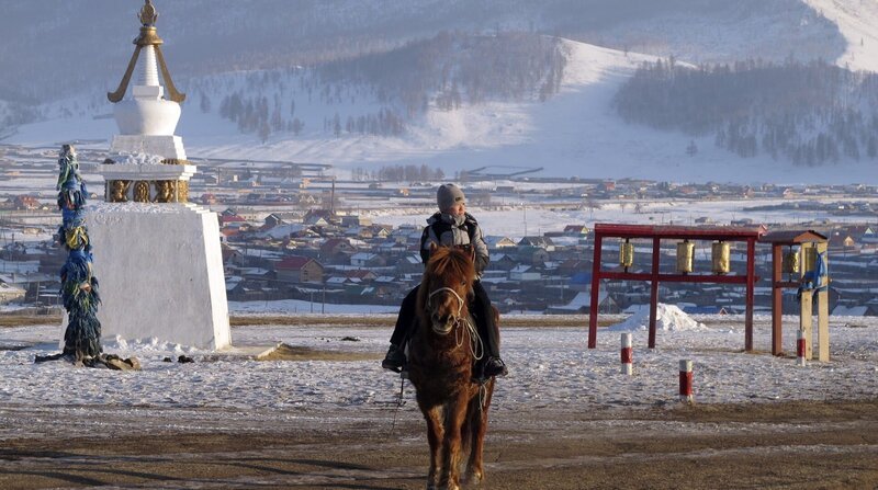 Der Nomadenjunge Tuguldur reitet nach der Schule nach Hause. Im Hintergrund der Schulort Tunkhel, 200 Kilometer nördlich der Hauptstadt Ulan Bator – Bild: Karsten Scheuren