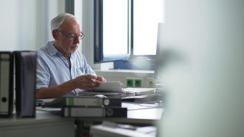 Heinz Steinmann kämpft sich immer wieder durch die Aktenberge, um eine Spur zu finden. – Bild: Benedikt Völler