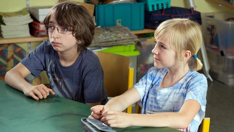 Gustav (Nikolaj Wolf) und Nelly (Jule Marleen Schuck) folgen gespannt dem Treiben ihrer Klassenkameraden. – Bild: SWR/​Maria Wiesler