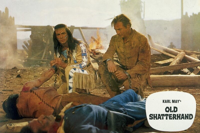 Winnetou (Pierre Brice) und Old Shatterhand (Lex Barker) knien vor dem toten Tujunga (Alain Tissier), der sich mit dem Pulvermagazin von Fort Grand selbst in die Luft gesprengt hat, um seinem Stamm den Sieg zu sichern. – Bild: Dicifrance