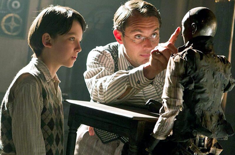 Hugo Cabret – Bild: Paramount /​ Hugo Cabret (Asa Butterfield, li.) hat schöne Erinnerungen an seinen Vater (Jude Law, Mi.), der Uhrmacher war, – etwa, wie der Vater einen Automatenmenschen repariert, den er später an Hugo vererbte.