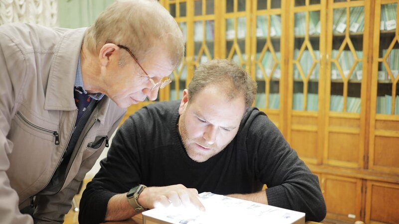 Josh Gates (r.) untersucht zusammen mit dem Historiker Yuri Kuntsevich Artefakte aus dem Dyatlov Pass Incident – Bild: Warner Bros. Discovery