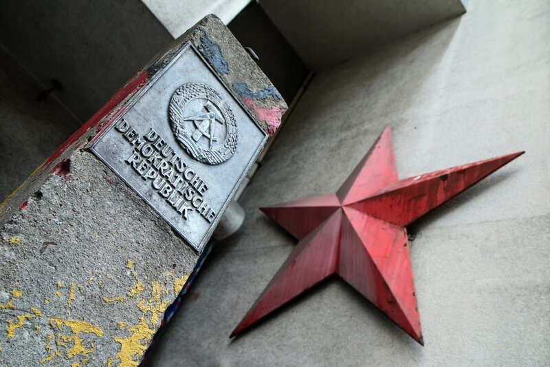 Das Detail eines Grenzsteins in Berlin mit dem Logo der Deutschen Demokratischen Republik und einem roten Sowjetstern an der Hausfassade. – Bild: Depositphotos