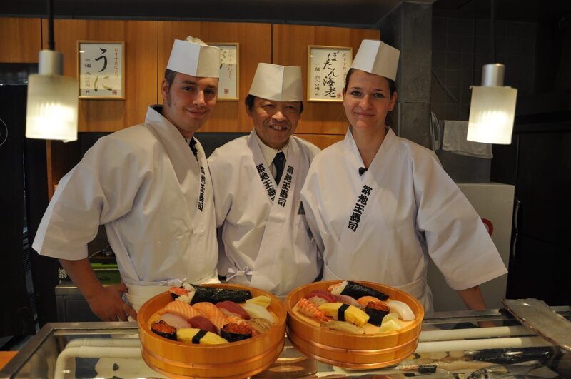 Patisserie-Praktikantin Agnes und Sous-Chef Philipp lernen den Sushi-Meister kennen und werden mit Kochschürzen und Mützen ausgestattet. – Bild: Bewegte Zeiten Filmproduktion GmbH/​BR/​Christian Hattesen