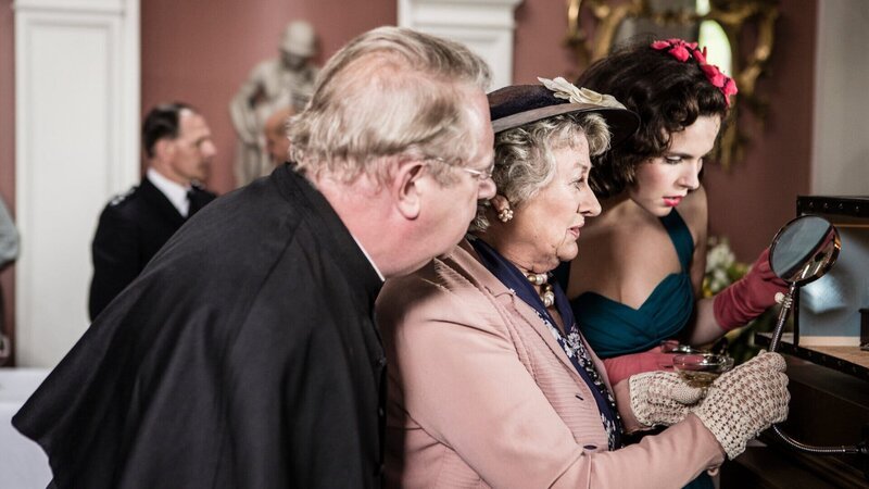 Mrs McCarthy (Sorcha Cusack, M.), Father Brown (Mark Williams, l.) und Bunty (Emer Kenny, r.) bewundern die detailgetreue Darstellung der Morde in den Dioramen. – Bild: Gary Moyes