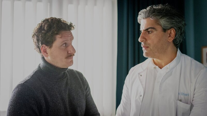 Sashas Mann Philipp (Dominik Weber, l.) vertraut sich Dr. Sharif (Atheer Adel, r.) an: Seine Frau ist ein Workaholic und will trotz Beinahe-Tod sofort wieder ihren Manager-Job aufgreifen, als sei nichts gewesen. – Bild: Boris Laewen, ZDF