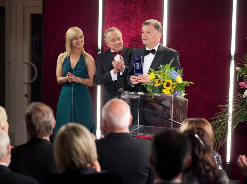 Dr. Roland Heilmann (Thomas Rühmann, rechts) bekommt von Prof. Simoni (Dieter Bellmann, Mitte) und einer Hostess (Komparsin) den Pasteurpreis verliehen. Seine Dankesrede widmet Roland vor versammeltem Publikum seiner Frau Pia – doch diese sucht er vergeblich unter den Zuhörern. – Bild: MDR/​MDR/​Rudolf Wernicke