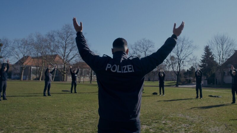 Polizeianwärterinnen und Polizeianwärter mit Polizeianwärter Yasin Khalife (M.) bei gemeinsamen Dehnübungen. – Bild: ZDF und Lisa Jilg
