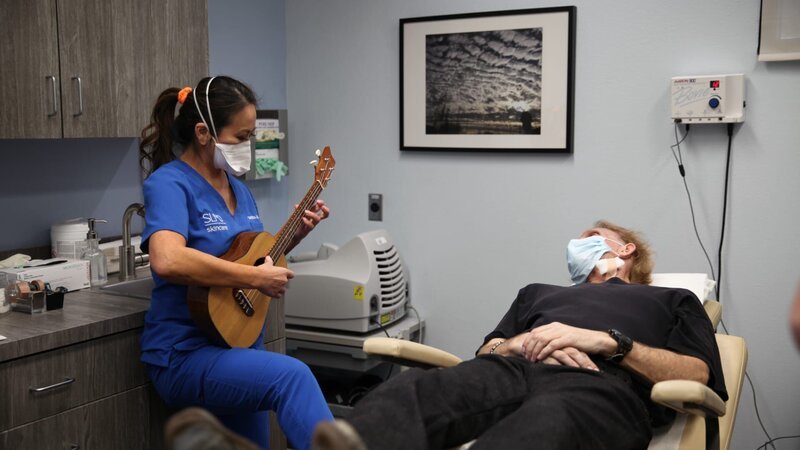 Dr. Lee spielt ihre Ukulele für Jerry Harrison nach dessen Lipom-Entfernung an der Wange. – Bild: Discovery Communications, LLC