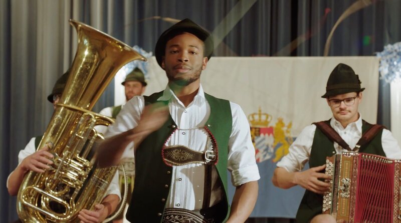 Der Flüchtling Alfons Nkmura (Dimitri Abold) darf die Goaßlschnalzer in den prestigeträchtigen Wettkampf führen. – Bild: ARD/​Lucky Bird Pictures/​Savoy Film Productions