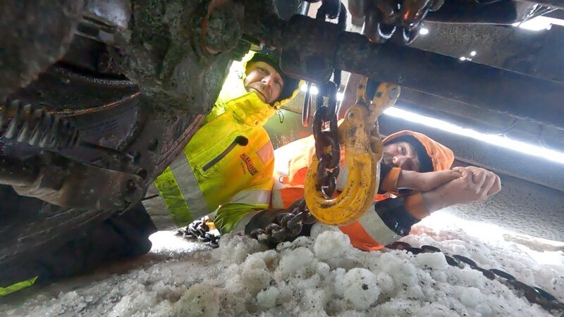 Bjoern and Thord work together under the truck to secure chains and get it ready for a tow out. – Bild: National Geographic